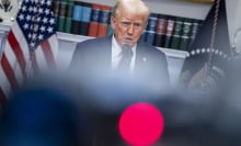 Trump stands at a podium surrounded by blurred out cameras and press members.