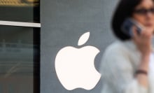 A woman, blurred in the foreground, walks by an Apple store.