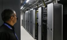 A man stands looking at a bank of AI data processors.