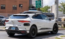 A Waymo midsize SUv parks in a lot in front of a "permit only" sign.