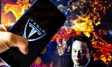 Tesla logo on mobile device with Elon Musk in the background