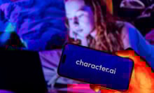 A child looks at a computer with a phone in the foreground bearing the Character.AI logo.