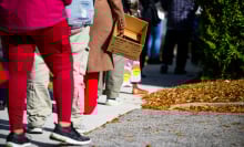 People stand in line holding cardboard boxes and grocery bags. 