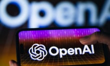A thumb taps on a phone screen displaying a colorful OpenAI logo.