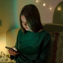 Sitting in her bedroom, a teen girl looks down at her phone. 