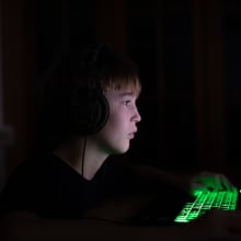 A tween or teen boy looks at a computer screen in a darkened room. 