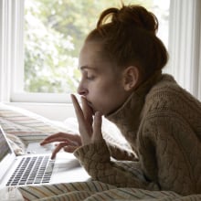 Teen girl looks at laptop computer while lying on her bed. 