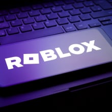 A phone displaying the Roblox logo in dark moody lighting.