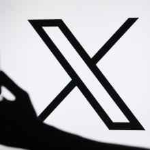x logo behind a hand holding a phone