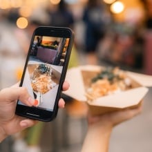 A woman takes a photo of her food at a market using a smartphone.