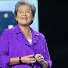 AMD CEO Lisa Su smiling on stage in front of an image of a Ryzen chip.