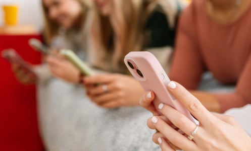 Girls sit in a row looking at their phones.