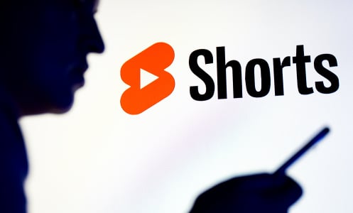 A person stands in profile staring at a phone. A large YouTube Shorts logo glows behind them. 