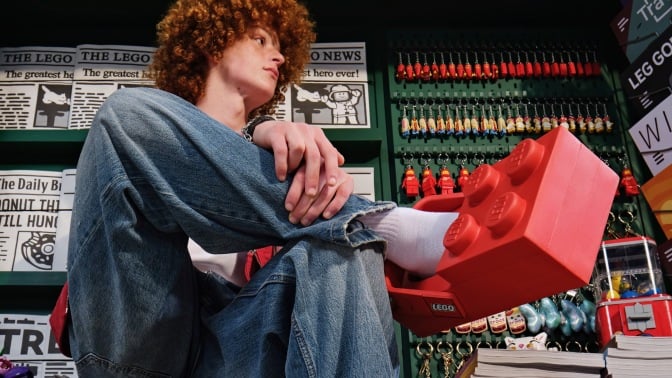 young man wearing lego brick clogs in front of a newstand