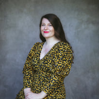 Rachel Thompson, sits wearing a dress with yellow florals and black background. 