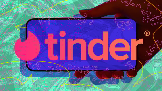 Hand holding phone with Tinder logo against abstract background