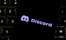 The Discord logo on a smart phone, resting on a computer keyboard.