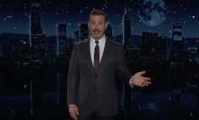 A man in a suit stands on a talk show stage.