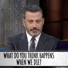 A man in a suit sits on a talk show. A question on the screen reads, "What do you think happens when we die?"