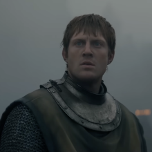 A man in armour sits on top of a horse on a battle field.