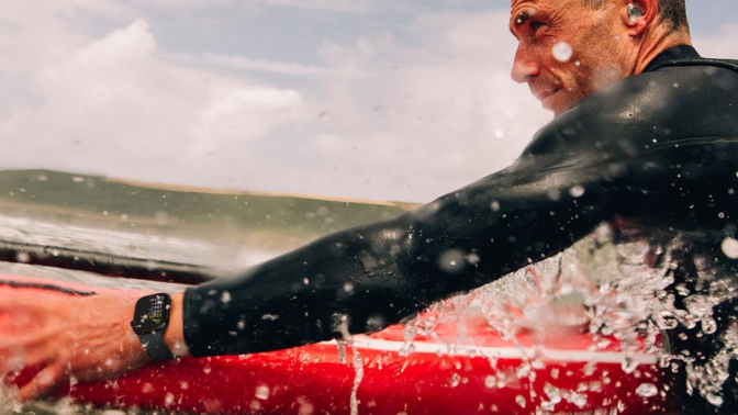 man in ocean with surfboard wearing apple watch